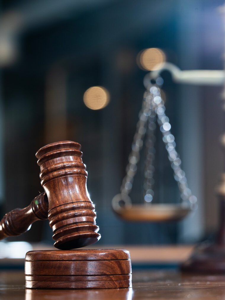 Ein Richterhammer aus dunklem Eichenholz. Im Hintergrund eine Schalenwaage leicht unscharf