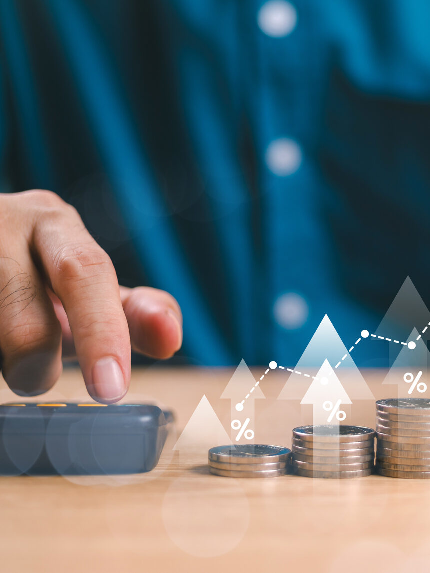 Hand tippt auf Taschenrechner, rechts daneben verschieden hohe Münzstapel