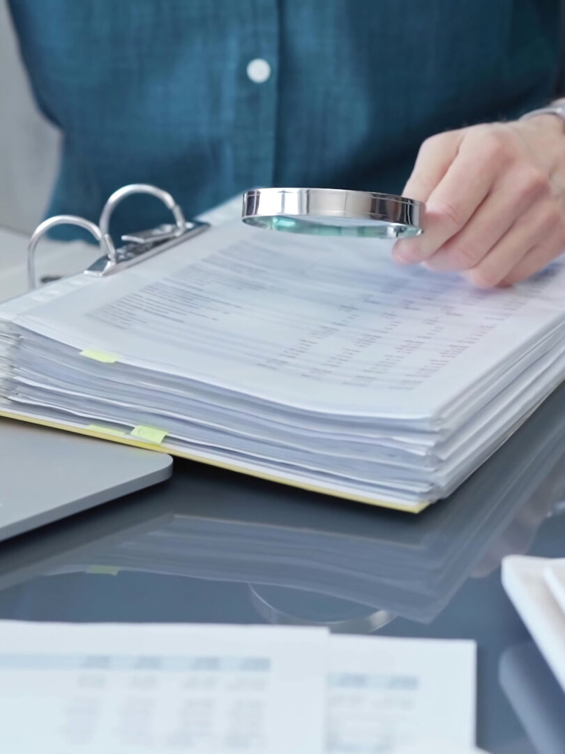 Hand hält Lupe um Tabellen in einem Ordner zu vergleichen