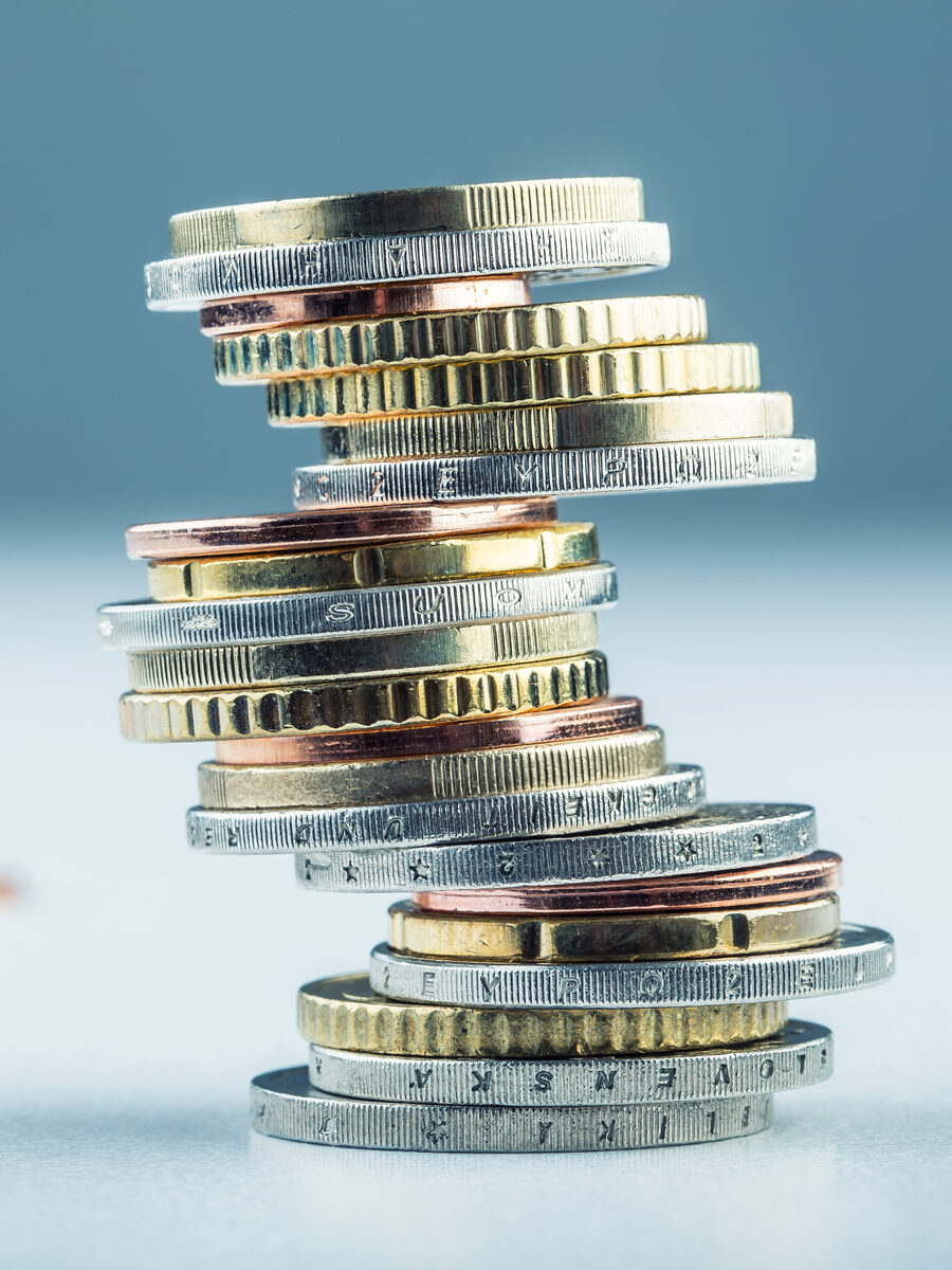 Stapel mit verschiedenen Münzen in Gold, Silber und Kupfer. Die Münzen liegen versetzt übereinander, der Stapel scheint wackelig